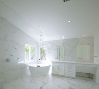 A bright, luxurious bathroom features white marble walls and floor. It includes a freestanding tub, a large shower, and a double vanity, highlighting modern elegance.
